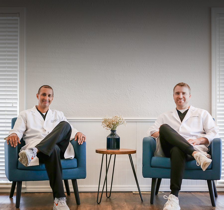 Two dentists in white coats sitting in teal chairs in modern office waiting room.