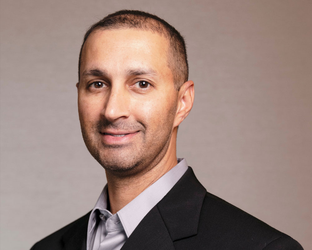 Portrait of Dr. Tej Lad Smiling and Wearing a Suit with a Soft Brown Background at One Eleven Dental Care