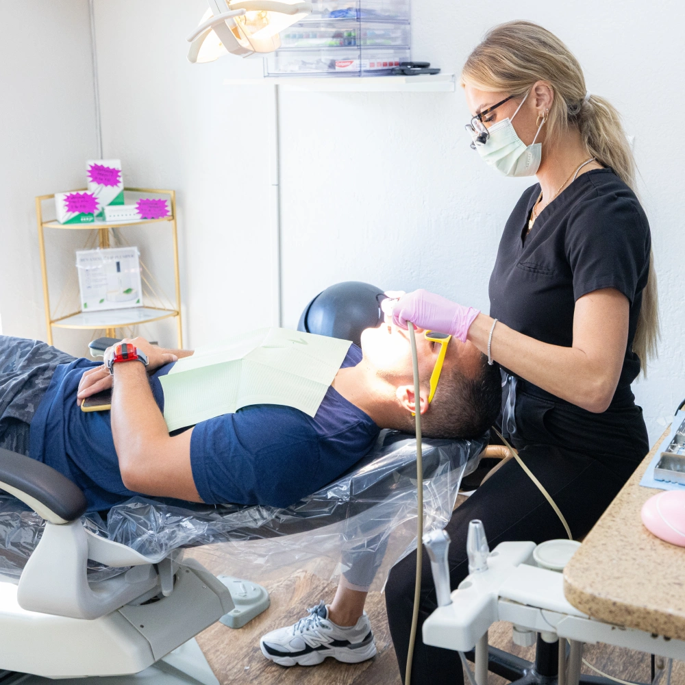 Dentist in mask examines patient's teeth in modern dental office treatment chair.